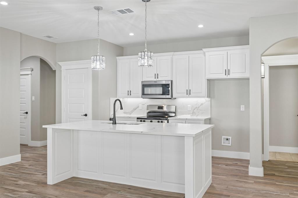 Kitchen featuring white cabinetry, quartz countertops with a waterfall-edge island, wood-finish flooring, matte black faucet, and arched doorways