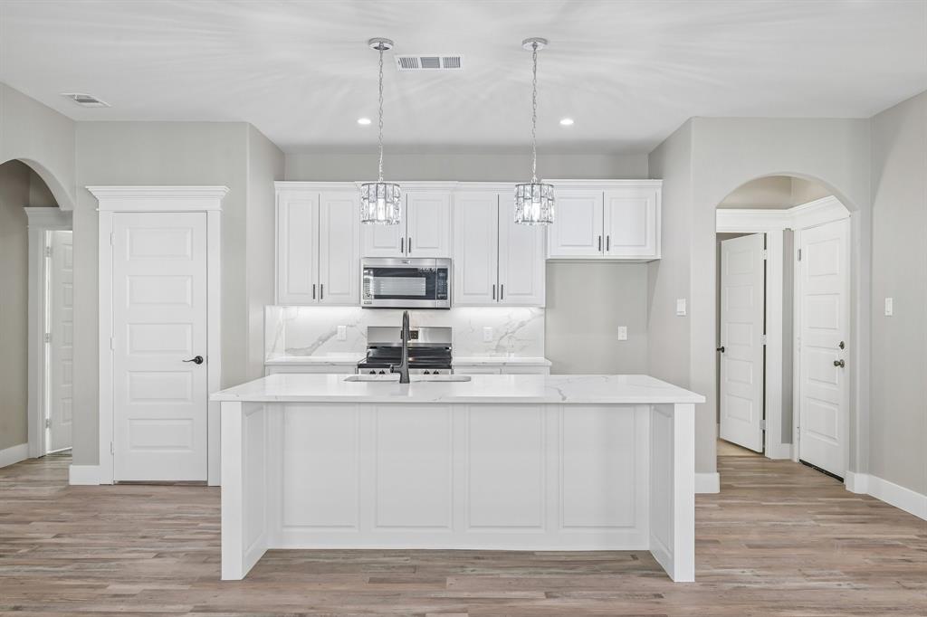 Kitchen featuring white shaker-style cabinetry, quartz countertops with a waterfall-edge island, stone-patterned backsplash, wood-finish flooring, and dual glass pendant lights
