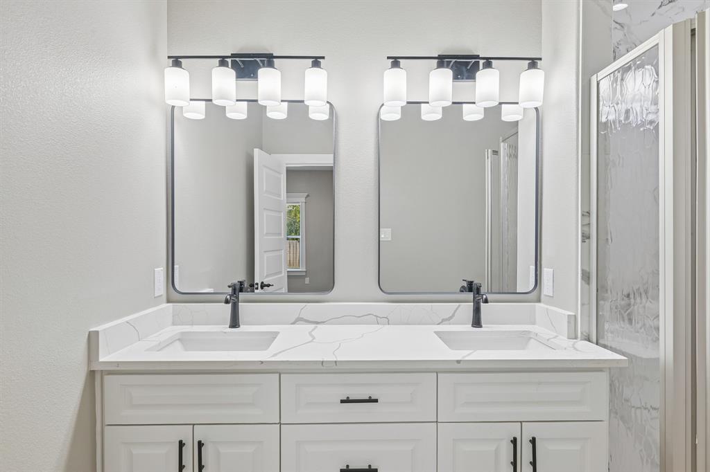Double vanity with white cabinetry, matte black hardware, stone-patterned countertop with integrated sinks, dual rectangular mirrors, and multi-light fixtures