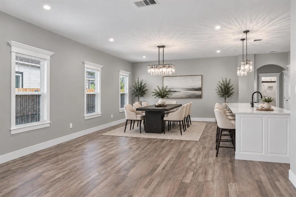 Open-concept interior featuring wood-finish flooring, recessed lighting, a rectangular tiered crystal chandelier, a center island with white cabinetry and a stone countertop, and multi-pane windows with detailed trim Open-concept interior featuring wood-finish flooring, recessed lighting, a rectangular tiered crystal chandelier, a center island with white cabinetry and a stone countertop, and multi-pane windows with detailed trim