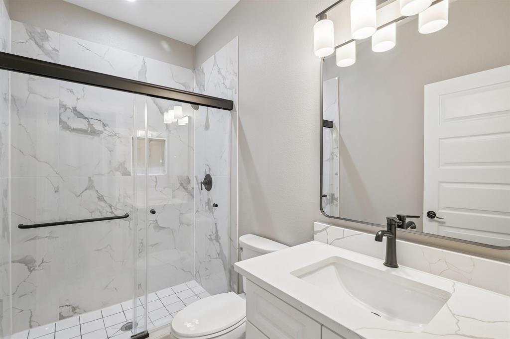 Bathroom featuring a vanity with a white countertop, a walk-in shower with floor-to-ceiling tiled walls and a glass enclosure, matte black fixtures, and a framed mirror