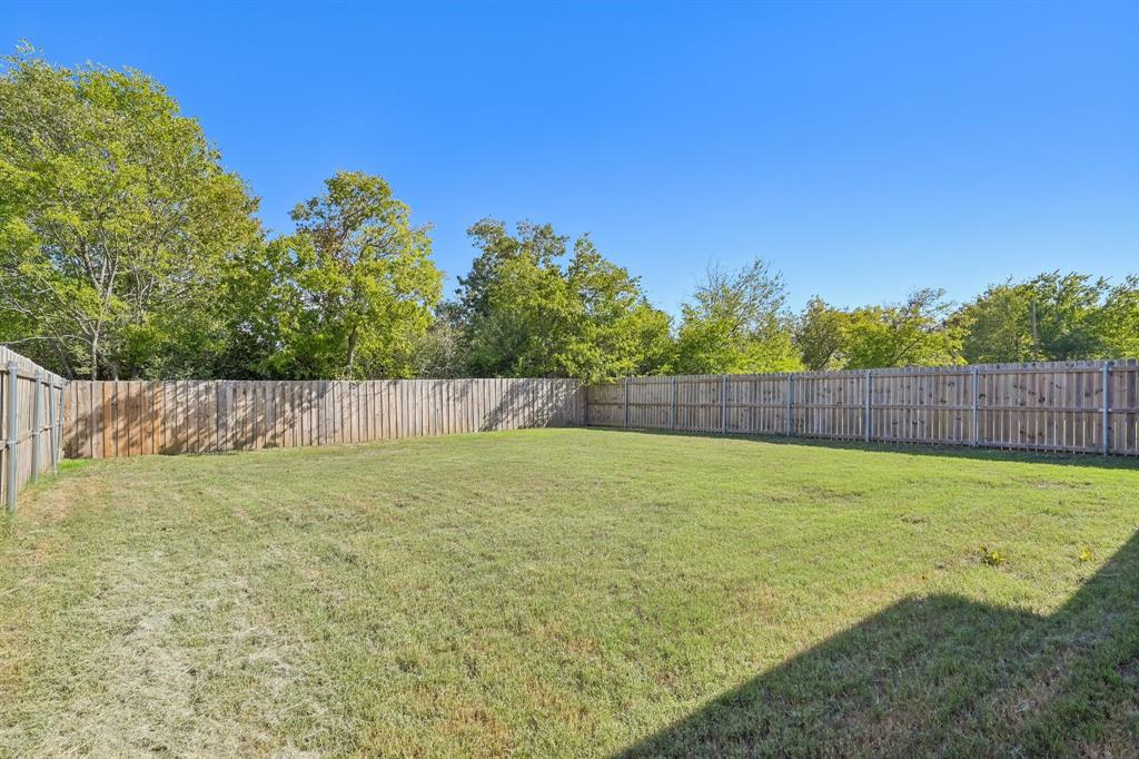 Expansive backyard featuring a level grass lawn, perimeter wood privacy fencing, and mature trees