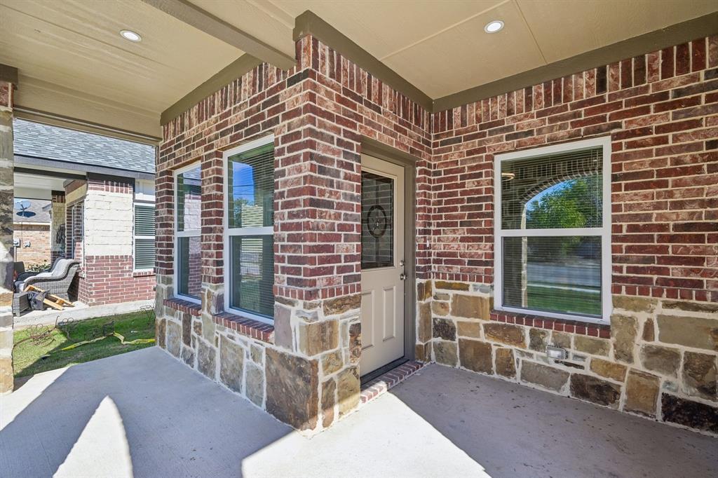 Covered entryway featuring a multi-textured exterior of mixed brick and stone masonry, recessed ceiling lighting, and a single-light panel front door Covered entryway featuring a multi-textured exterior of mixed brick and stone masonry, recessed ceiling lighting, and a single-light panel front door