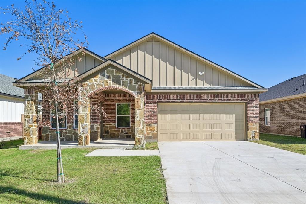 Single-story exterior featuring a brick and stone facade, vertical siding accents, an arched covered entryway, and a concrete driveway leading to an attached two-car garage Single-story exterior featuring a brick and stone facade, vertical siding accents, an arched covered entryway, and a concrete driveway leading to an attached two-car garage