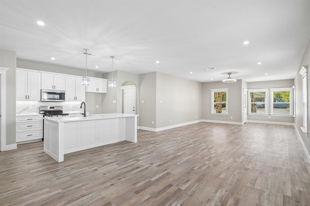 Open-concept kitchen featuring white shaker-style cabinetry, quartz countertops, a central island, wood-finish flooring, and recessed lighting