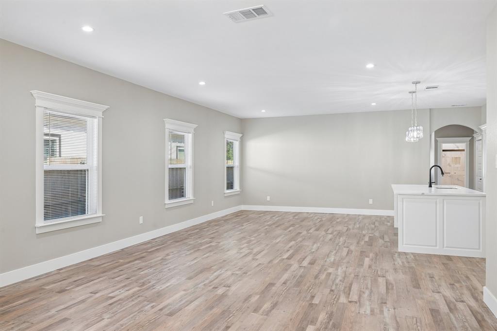 Open-concept interior featuring wood-finish flooring, recessed lighting, neutral wall tones, multi-pane windows with detailed trim, and a built-in island with a matte black faucet