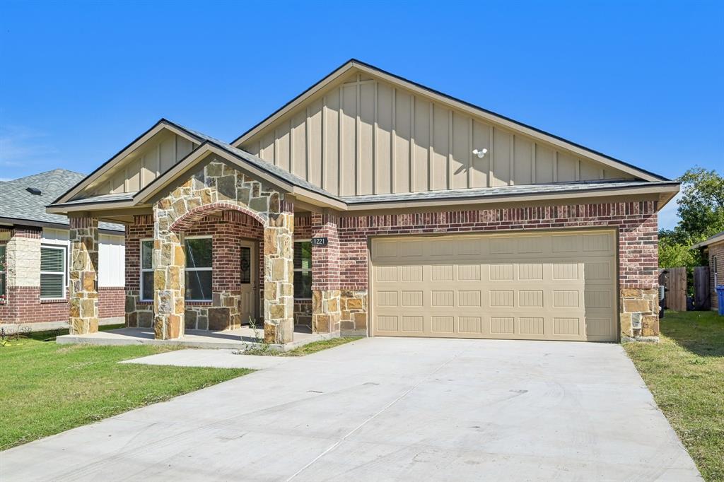 Exterior featuring brick and stone masonry, vertical siding, a covered entryway with a stone-clad arched porch, and a two-car garage Exterior featuring brick and stone masonry, vertical siding, a covered entryway with a stone-clad arched porch, and a two-car garage