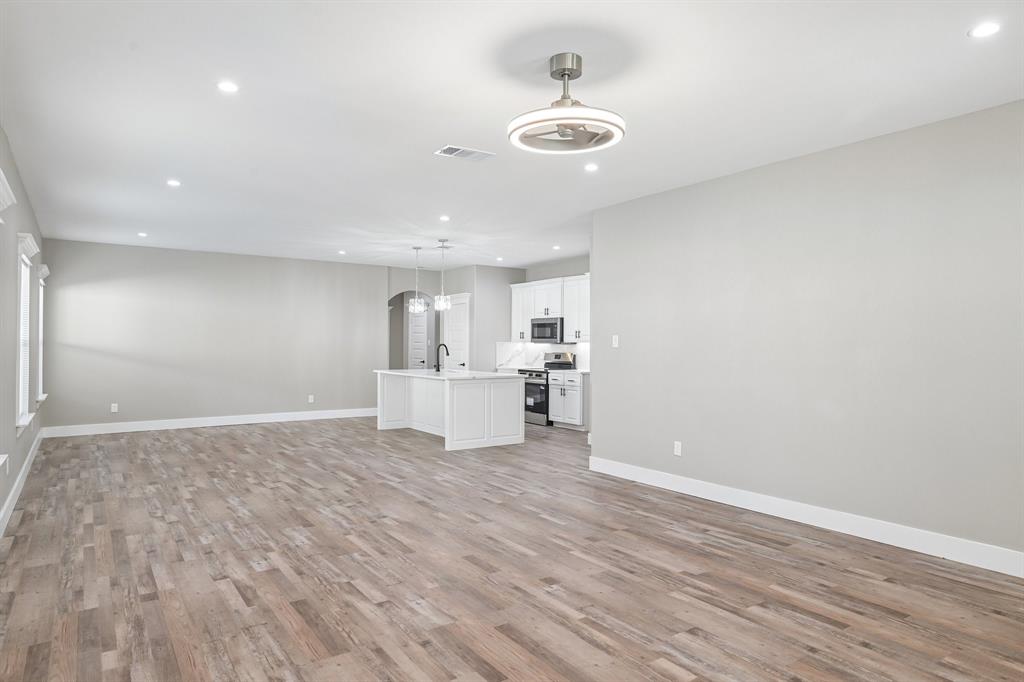 Open-concept interior featuring wood-finish flooring, recessed lighting, a modern ceiling fan, and a kitchen equipped with a central island and white cabinetry Open-concept interior featuring wood-finish flooring, recessed lighting, a modern ceiling fan, and a kitchen equipped with a central island and white cabinetry