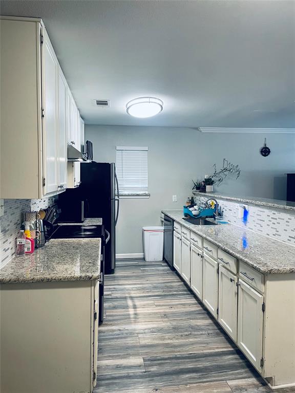 Kitchen featuring stone-finish countertops, white cabinetry, wood-finish flooring, and decorative tile backsplash Kitchen featuring stone-finish countertops, white cabinetry, wood-finish flooring, and decorative tile backsplash