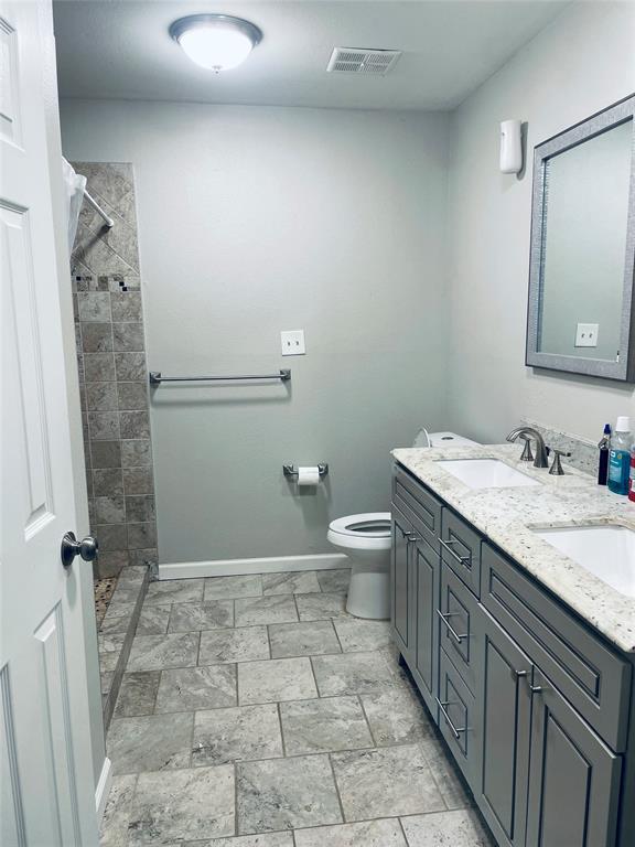 Bathroom featuring a dual-sink vanity with a stone countertop, tile flooring, and a walk-in shower with tiled walls