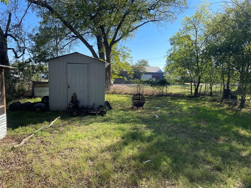Grassy backyard area featuring mature trees, perimeter chain-link fencing, and a detached storage structure