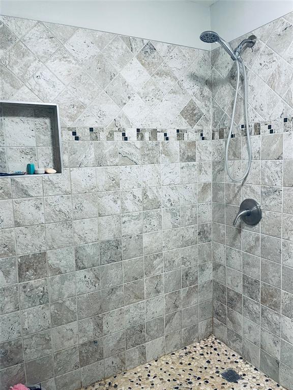 Shower enclosure featuring stone wall tile in a diamond and square pattern, decorative mosaic tile accent, built-in recessed wall niche, and handheld shower fixture