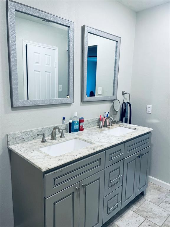 Dual-sink vanity with light-toned stone countertop, rectangular undermount basins, brushed-metal hardware, and decorative framed mirrors