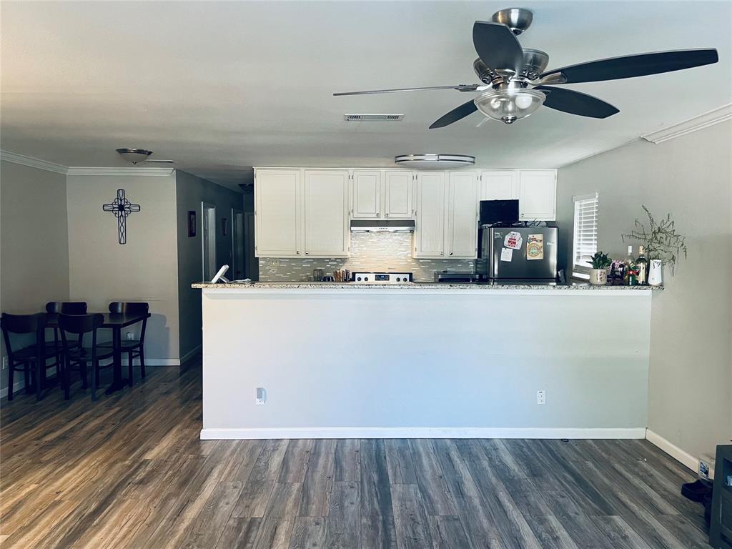 Kitchen featuring white cabinetry, stone-finish countertops, tile backsplash, wood-finish flooring, and a ceiling fan with integrated lighting Kitchen featuring white cabinetry, stone-finish countertops, tile backsplash, wood-finish flooring, and a ceiling fan with integrated lighting