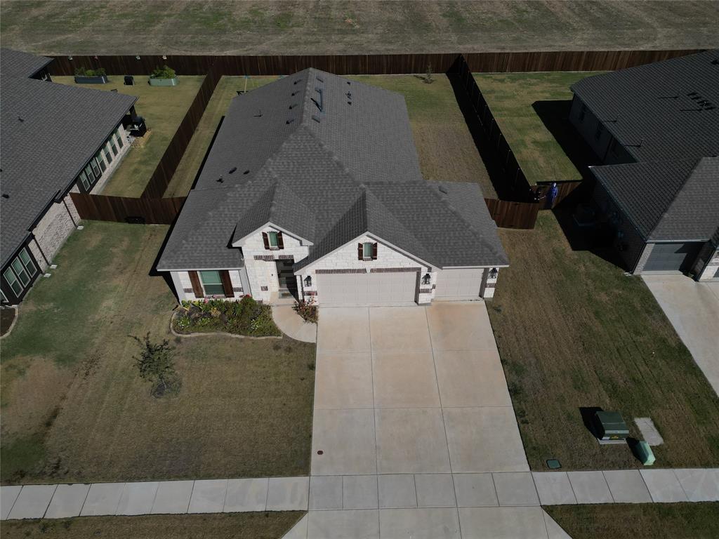 Aerial perspective of a brick and stone veneer exterior featuring a multi-gable roofline, attached three-car garage, concrete driveway, and full privacy wood fencing