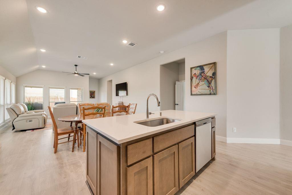 Kitchen island featuring light-toned cabinetry, quartz countertops, an undermount stainless steel sink, and recessed lighting throughout the room