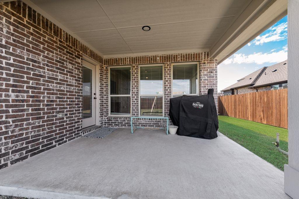 Covered concrete patio featuring brick exterior walls, multiple windows with blinds, and a fenced backyard
