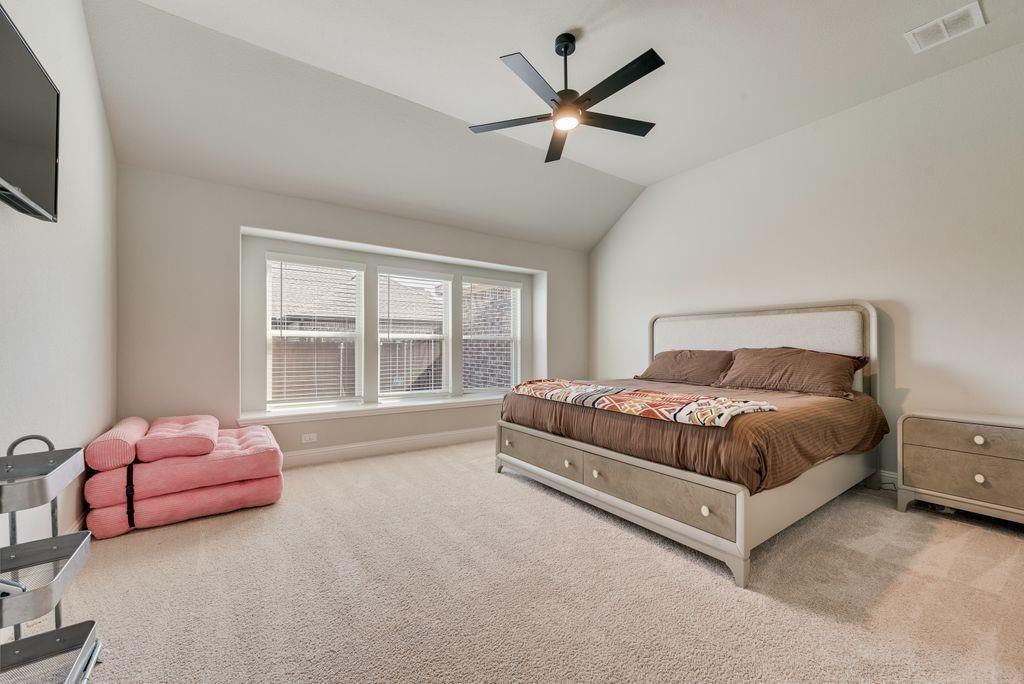 Vaulted ceiling, neutral wall tones, wall-to-wall carpeting, expansive triple-pane window, and matte black ceiling fan with integrated lighting