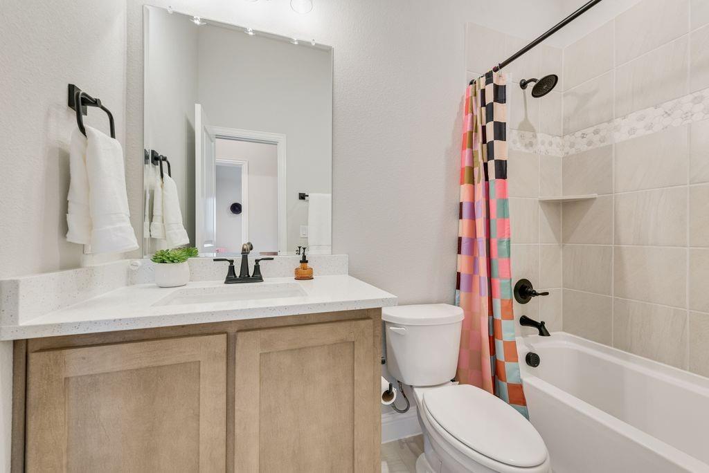 Bathroom featuring a wood-finish vanity with a stone countertop, an integrated rectangular sink, matte black hardware, and a tub-shower combination with ceramic tile surround