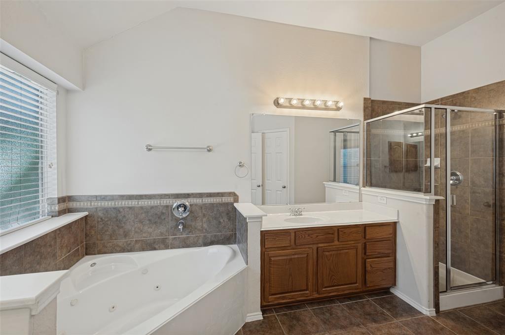 Corner jetted tub with tile surround, wood cabinetry vanity, integrated sink, and glass-enclosed shower with tile wall finish
