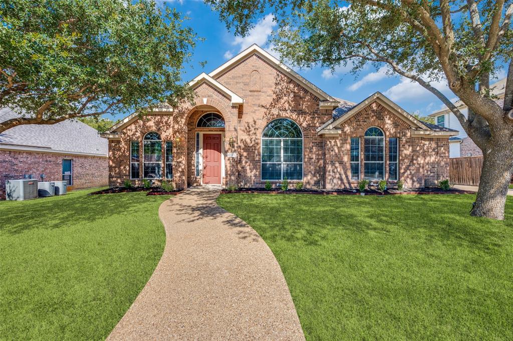 Single-story brick exterior featuring an arched entryway, decorative transom windows, a concrete aggregate walkway, and mature landscape trees