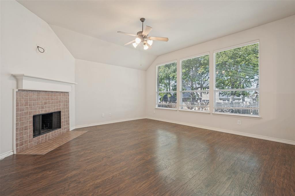 Vaulted ceilings, wood-finish flooring, fireplace with a tile surround and mantel, and large windows with integrated blinds
