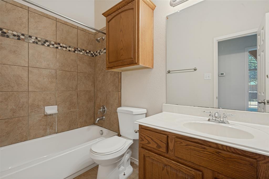 Bathroom featuring a vanity with a white countertop and oval under-mount sink, wood-finish cabinetry, wall-mounted storage cabinet, and a tiled shower surround with a decorative accent border