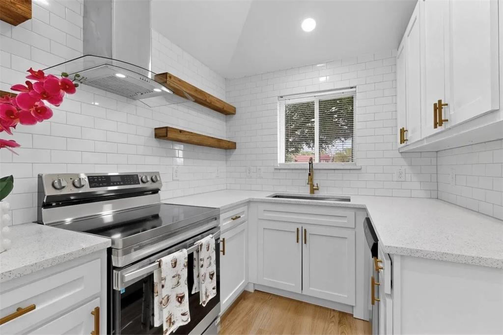 Kitchen featuring white shaker-style cabinetry, quartz countertops, white subway tile backsplash, stainless steel range with integrated exhaust hood, and wood-finish open shelving