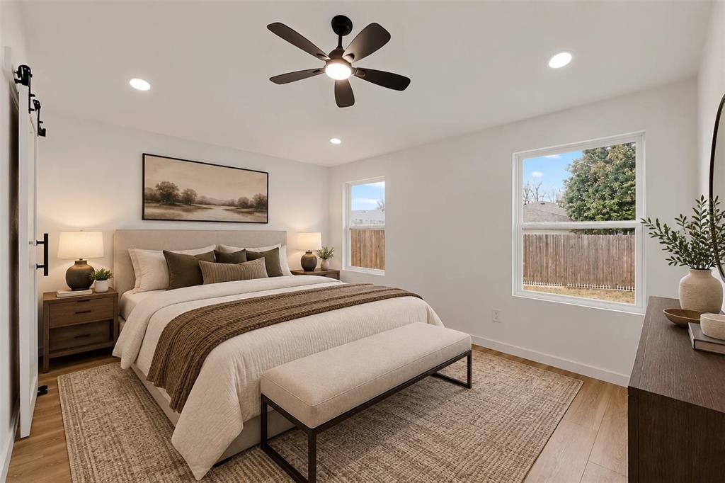 Neutral interior featuring wood-finish flooring, recessed lighting, a matte black ceiling fan, and sliding barn-style door hardware