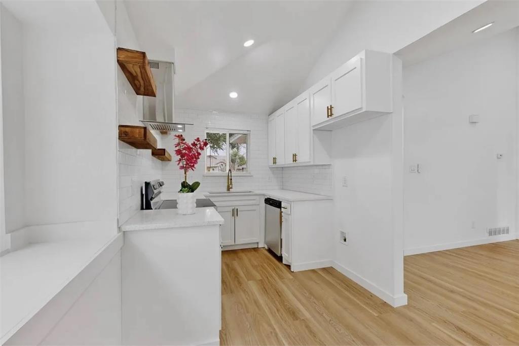 Kitchen featuring white cabinetry, subway tile backsplash, wood-finish flooring, stainless steel range hood, and wood-finish wall-mounted floating shelves