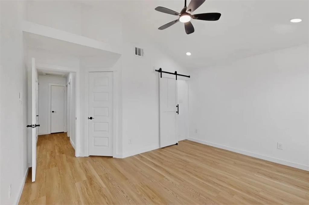 Interior space featuring vaulted ceilings, wood-finish flooring, a contemporary ceiling fan, and a white sliding barn door with matte black hardware