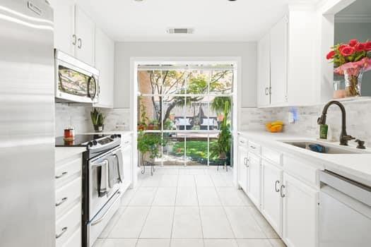 Kitchen featuring white shaker-style cabinetry, stainless steel appliances, tile flooring, stone-tiled backsplash, and floor-to-ceiling glass sliding doors Kitchen featuring white shaker-style cabinetry, stainless steel appliances, tile flooring, stone-tiled backsplash, and floor-to-ceiling glass sliding doors