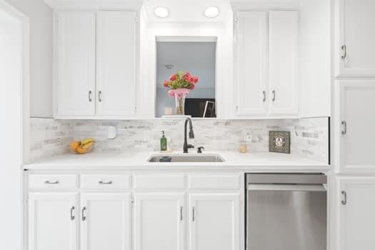 Kitchen featuring white cabinetry, stone-style tile backsplash, stainless steel dishwasher, matte black faucet, and recessed lighting Kitchen featuring white cabinetry, stone-style tile backsplash, stainless steel dishwasher, matte black faucet, and recessed lighting