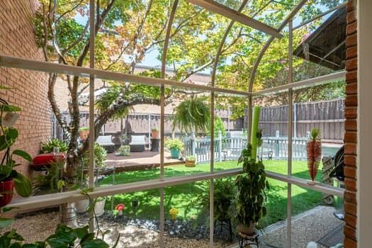 Enclosed sunroom featuring an arched metal-frame glass structure, exposed brick exterior wall, landscaped yard with lawn, raised wooden deck, and privacy fencing Enclosed sunroom featuring an arched metal-frame glass structure, exposed brick exterior wall, landscaped yard with lawn, raised wooden deck, and privacy fencing