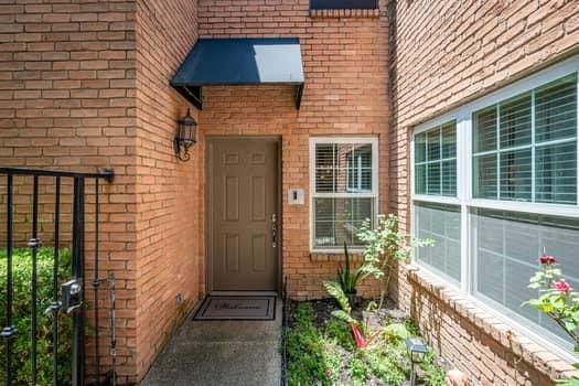 Brick exterior entrance featuring a metal awning, solid core six-panel door, exterior wall-mounted lantern, and grid-patterned windows Brick exterior entrance featuring a metal awning, solid core six-panel door, exterior wall-mounted lantern, and grid-patterned windows