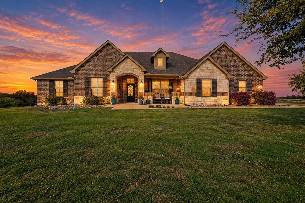 Single-story residence featuring a mixed-material facade of brick and cut stone, arched entryway, shingle roof, and dark decorative shutters