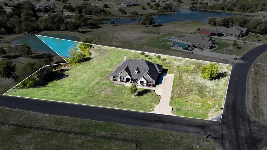 Aerial perspective of a detached residence featuring a multi-pitched roof, concrete driveway, and expansive acreage including a pond