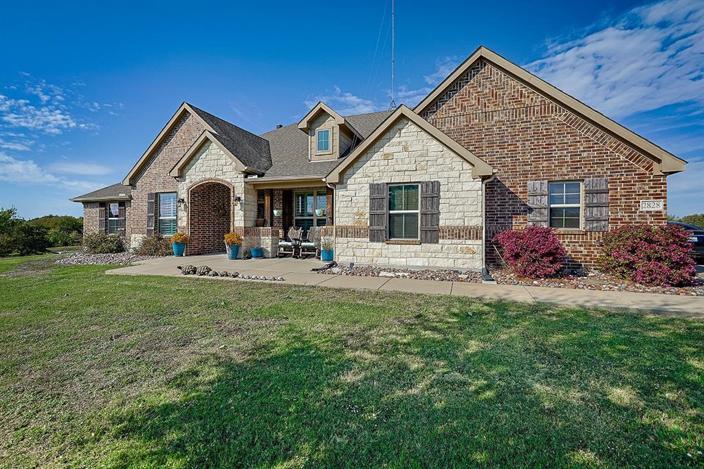 Multi-gabled exterior featuring a combination of brick and stone masonry, decorative shutter accents, a covered front entry with an arched brick header, and an expansive lawn