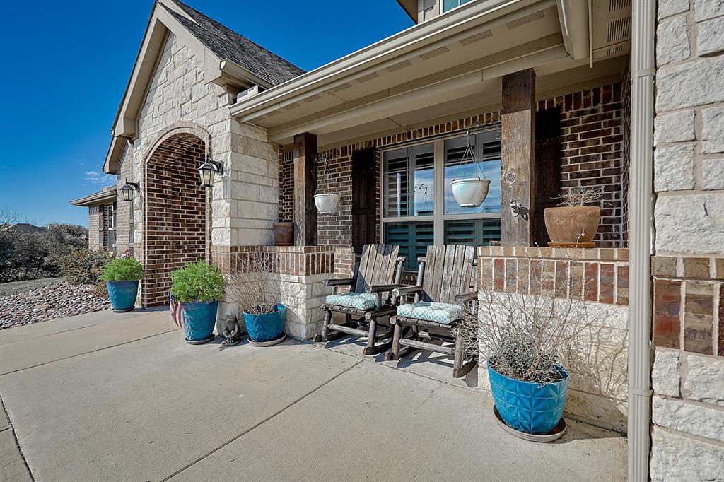 Covered entryway featuring a stone-clad archway, multi-textured brick and stone exterior, concrete porch, and decorative wood-finish structural posts