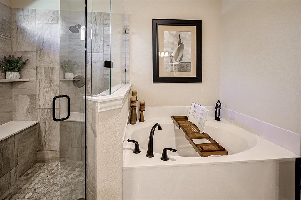 Soaking tub with a deck-mounted faucet, glass-enclosed shower featuring large-format tile surround, integrated bench seating, and pebble-finish shower floor