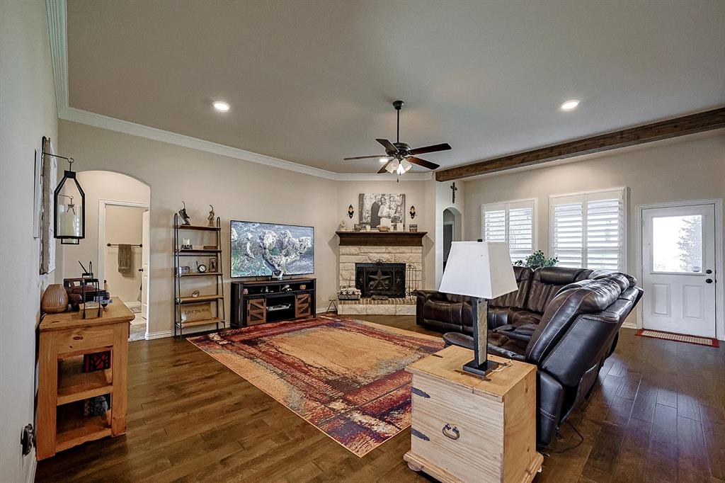 Living area featuring wood-finish flooring, stone fireplace with a dark wood mantel, recessed lighting, ceiling fan, and plantation shutters