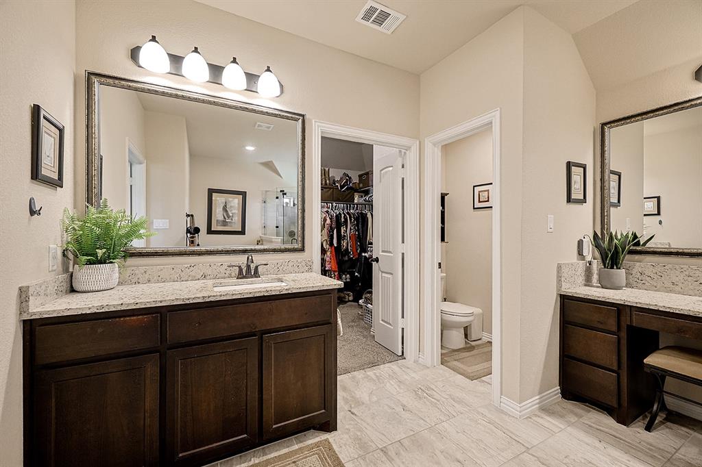 Bathroom featuring dark-finish wood cabinetry, speckled stone-surface countertops, dual rectangular under-mount sinks, large framed mirrors, and tile flooring