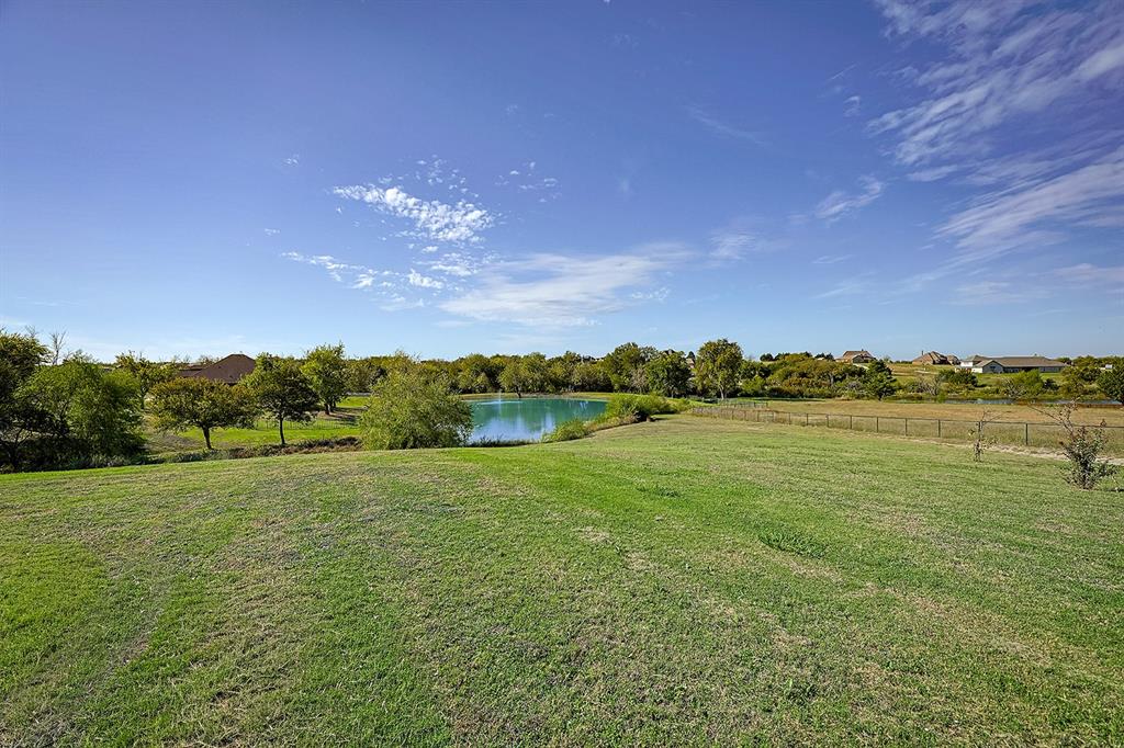 Expansive grounds featuring a manicured lawn, natural pond, mature trees, and perimeter fencing