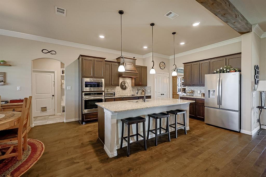 Kitchen featuring a center island with light-toned stone countertops, dark-stained wood cabinetry, stainless steel appliances, wood-finish flooring, and pendant lighting