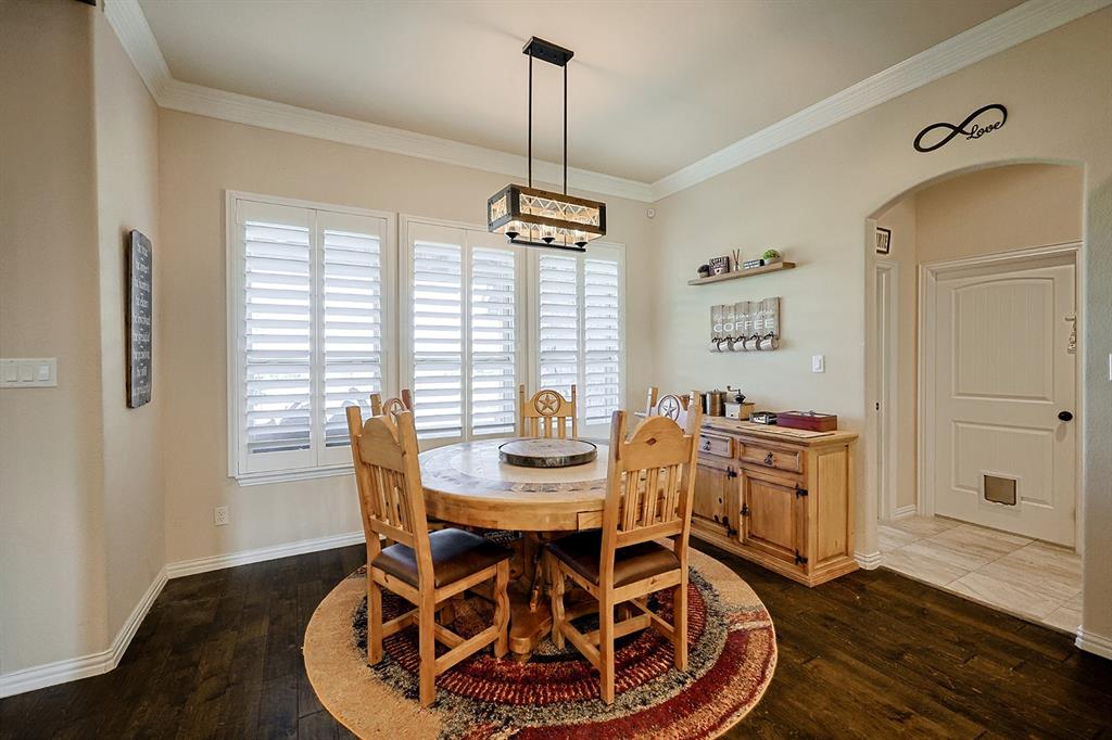 Dining area featuring wood-finish flooring, plantation shutters, crown molding, and a rectangular multi-light pendant fixture