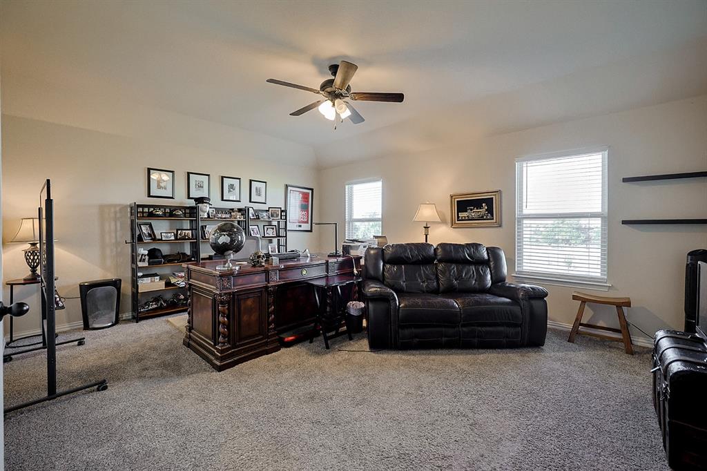 Neutral-toned carpeted interior featuring a vaulted ceiling, ceiling fan with integrated lighting, and dual wall-mounted floating shelves