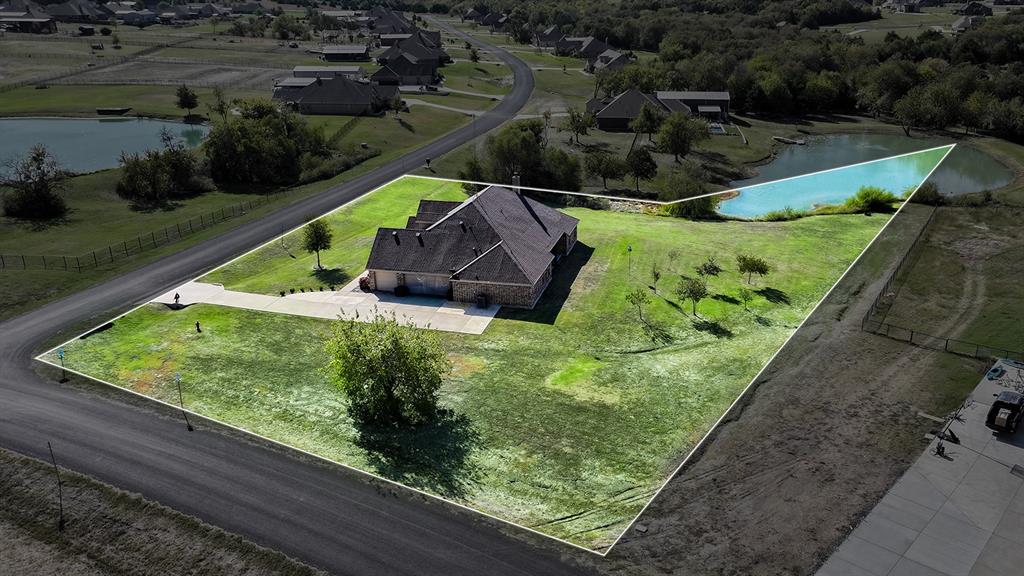 Aerial view of a residential property featuring a multi-pitched roofline, brick exterior, attached garage, expansive lot, and private pond access