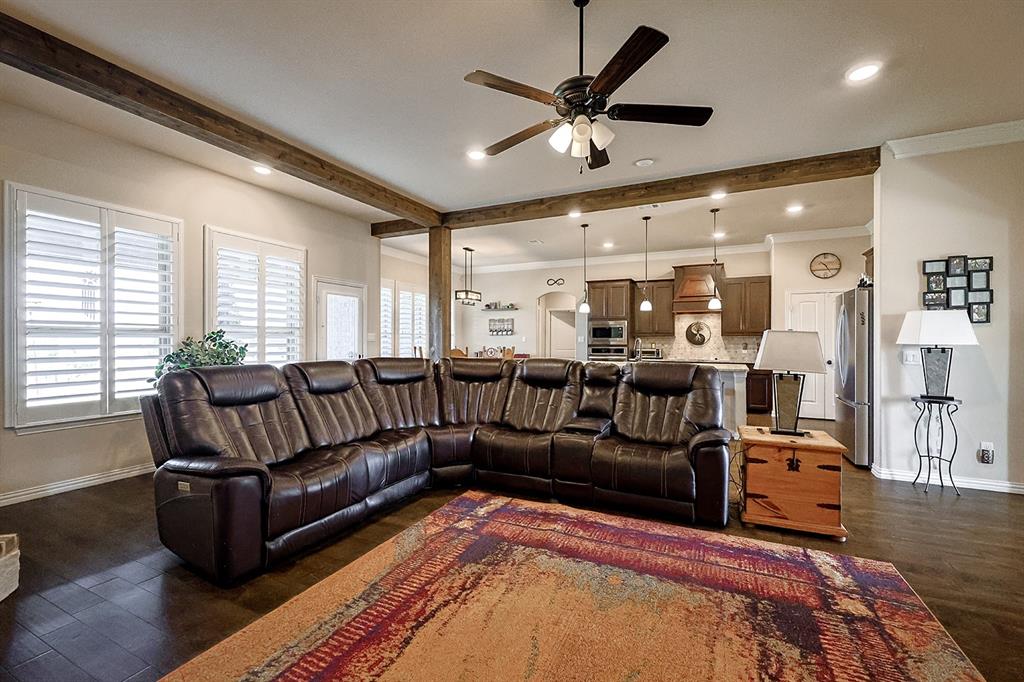 Open-concept interior featuring wood-finish flooring, decorative ceiling beams, plantation shutters, recessed lighting, and a kitchen island with pendant fixtures