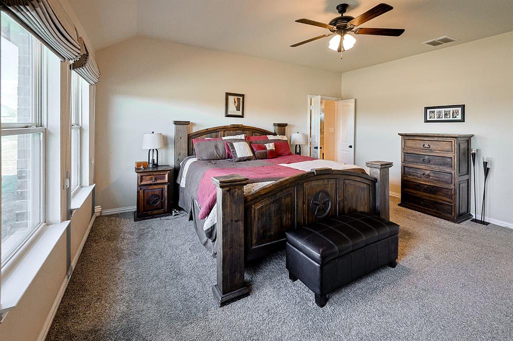 Vaulted ceiling featuring a ceiling fan with integrated lighting, neutral wall-to-wall carpeting, and large windows with decorative valances