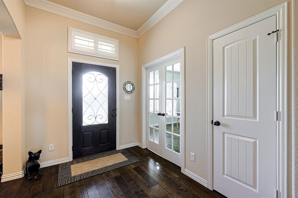 Foyer featuring wood-finish flooring, crown molding, a dark-finish entry door with decorative glass inlay, transom window with shutters, and dual French doors with glass panes